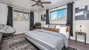 A bedroom with a large bed, a chair, a massage chair, and a ceiling fan.
