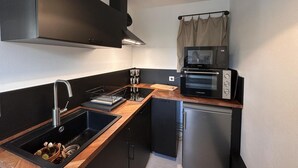 Une cuisine compacte équipée d  ’un évier, de meubles de rangement noirs, d’un four encastré et d’un petit réfrigérateur.