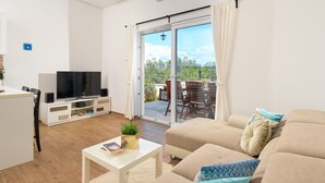 A living room with a sofa, a coffee table, a TV, and a sliding glass door leading to an outdoor area with a table and chairs. - Sun Spalato Villa Cikas (Murter-Kornati)