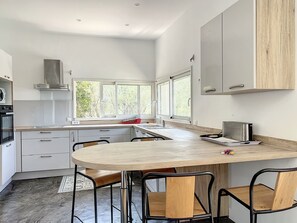A modern kitchen with a central island, white cabinetry, and a view of greenery outside.