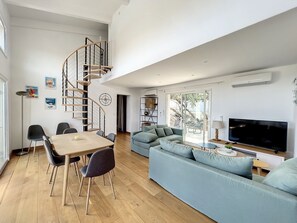 A spacious living area with a spiral staircase, a large sofa, a TV, and a dining table with chairs.