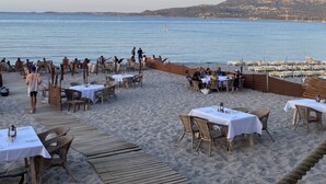 Un restaurant situé en bord de mer, avec une terrasse et des tables, offrant une vue sur l’océan.