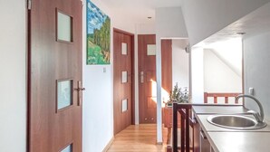 A narrow hallway with wooden doors, a kitchen area with a sink and wooden chairs, and a painting on the wall. - 4 bedroom amazing home in Parzensko (Parzensko)