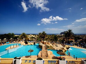 A resort pool area with clear blue water, palm trees, and a view of the city in the background. - Uniquely situated Holiday Bungalow in Calpe, Spain. 2 Bedrooms, 1 Bathroom (Calp)