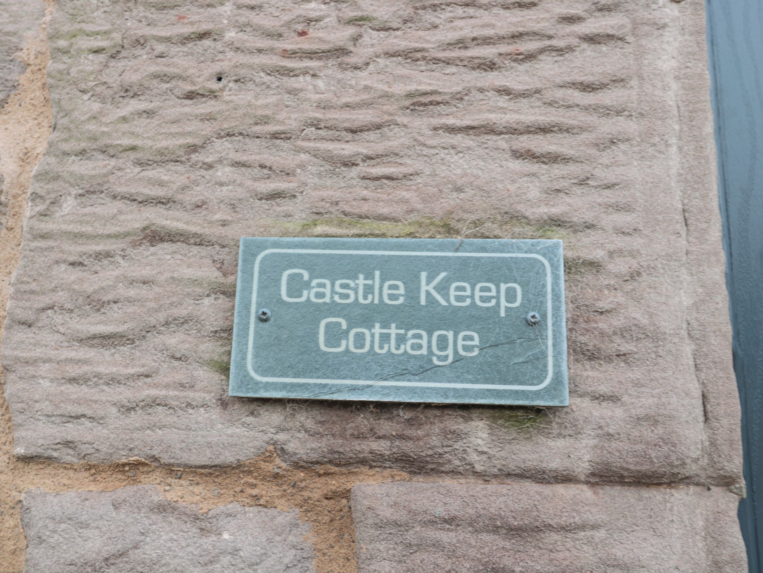 Un muro de piedra con un letrero que dice "Castle Keep Cottage".
