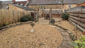 Un jardin agrémenté d’une pergola en bois, d’un chemin de pierres et d’un abreuvoir à oiseaux.