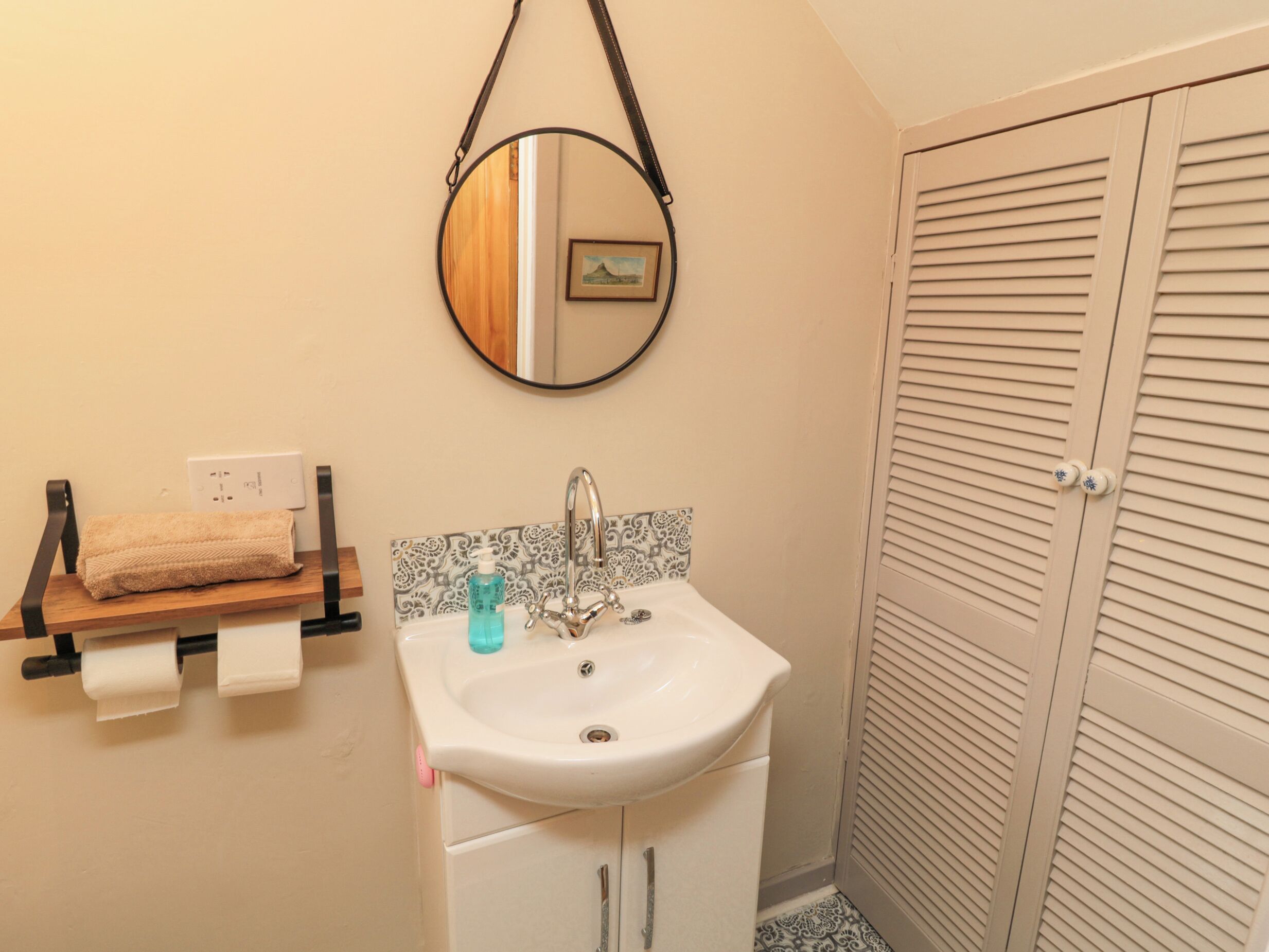 A bathroom with a sink, mirror, towel rack, and a door with louvered panels.