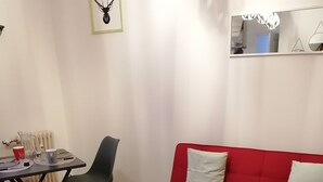 A living room with a red sofa, two red cushions, a small round table with a pair of sunglasses, and a herringbone-patterned rug.