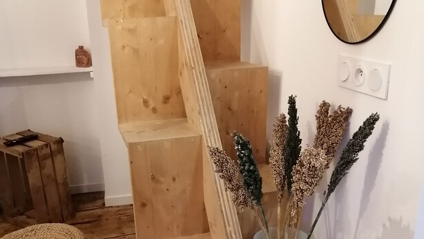 A wooden staircase with a blue vase of dried flowers on the landing.