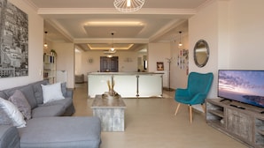 A modern living room with a grey sofa, a teal armchair, a coffee table, and a TV on a wooden stand. - Villa Serenity (Kropia)