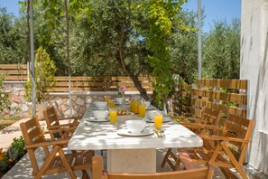 An outdoor dining area with a table set for breakfast, surrounded by wooden chairs and a stone wall. - Villa Serenity (Kropia)