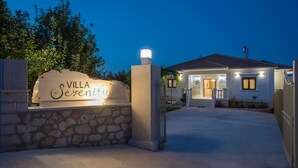 A villa named "Villa Serenity" with a stone entrance, a tiled roof, and a well-lit pathway leading to the entrance. - Villa Serenity (Kropia)