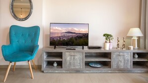 A living room with a teal armchair, a flat-screen TV, a wooden entertainment unit, a mirror, and a lamp. - Villa Serenity (Kropia)