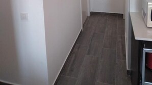 Ein schmaler Flur mit weißen Wänden, einer Tür am Ende und einer Mikrowelle auf einer Anrichte rechts.