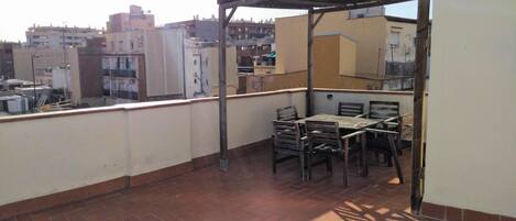 A rooftop terrace with a metal pergola, a table, and four chairs.