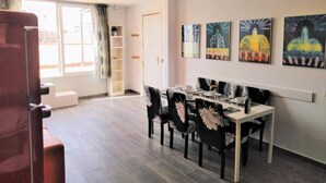 Ein Essbereich mit einem Tisch, gedeckt für vier Personen, umgeben von Stühlen mit Blattmustern. Über dem Tisch hängen vier gerahmte Kunstwerke an der Wand.