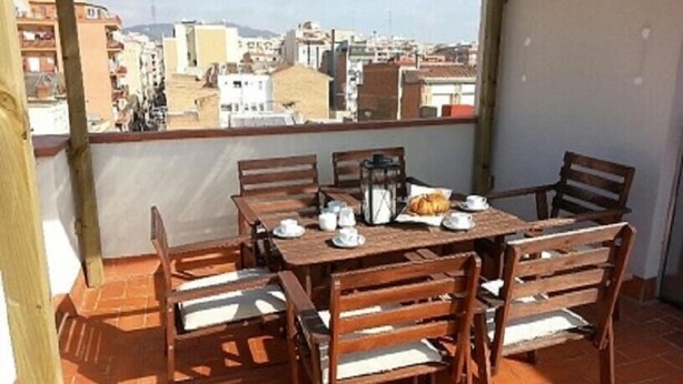 Eine Terrasse mit Tisch für vier Personen, umgeben von Holzstühlen mit Sitzkissen.