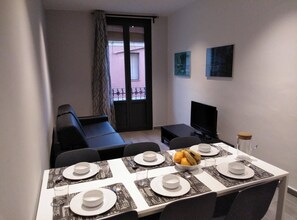 Ein Essbereich mit einem Tisch für vier Personen, einer schwarzen Couch, einem Fernseher und Kunstwerken an der Wand.