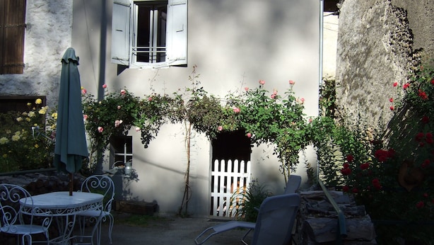 A patio with a white table and chairs, a white picket fence, and a climbing rose bush. - In the heart of a preserved, welcoming, flower-filled mountain village (La Fajolle)