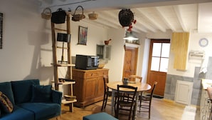 A cozy living room with a sofa, a coffee table, and a dining area with a table and chairs. There is a kitchen area with a microwave and cabinets. - In the heart of a preserved, welcoming, flower-filled mountain village (La Fajolle)