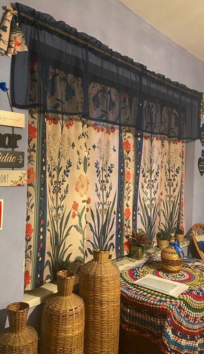 A room with a floral-patterned curtain, wicker vases, and a crocheted tablecloth.