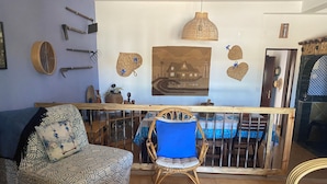 Una sala de estar con un sofá estampado, una silla de mimbre, una mesa de centro de vidrio y un comedor con mantel azul.