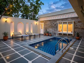 Zona de piscina con sillas reclinables, un muro de piedra y una ventana con vistas.