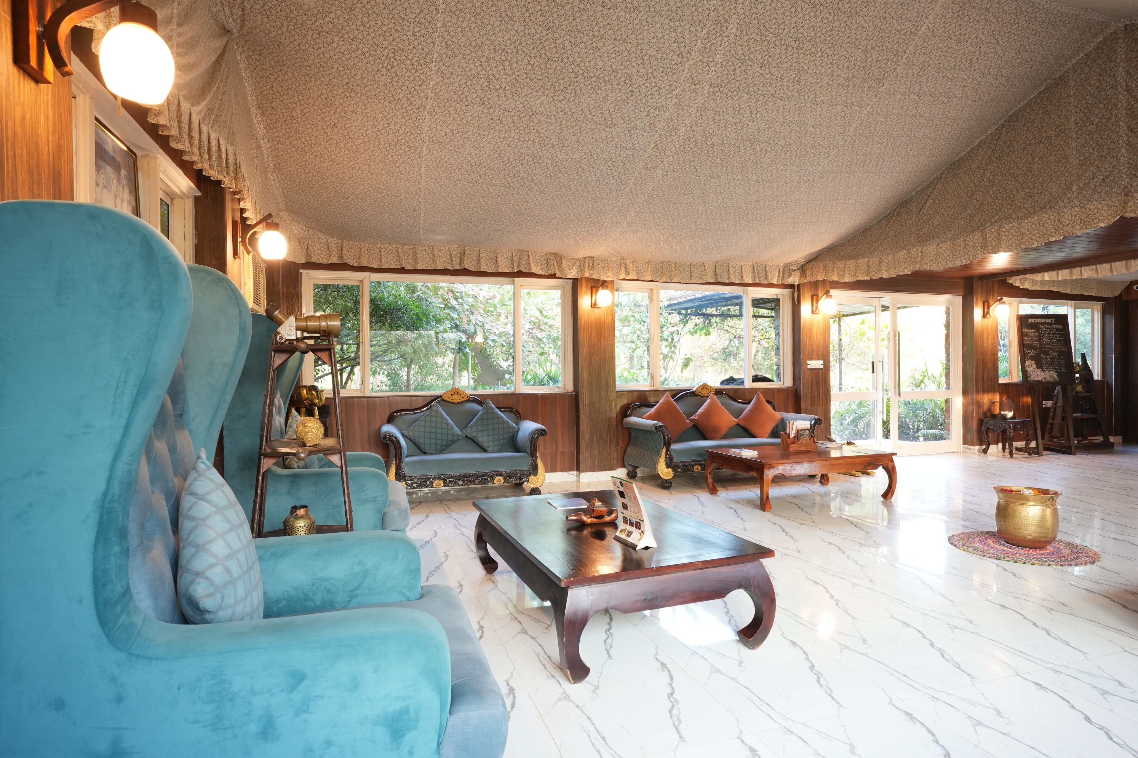 A spacious living room with a large blue sofa, a wooden coffee table, and a blue armchair. There are two sofas with cushions, a wooden side table, and a large window providing natural light.