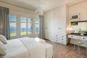 Quarto com uma cama grande, uma escrivaninha e uma cadeira. Há várias janelas e vista para o exterior.