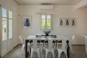Uma área de refeições com uma mesa e cadeiras brancas, uma planta em vaso e quadros nas paredes.