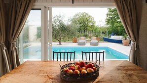 Een houten tafel met een fruitmand, een zwembad en terrasmeubels.