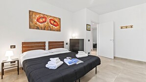 A hotel room with a bed, a painting, a lamp, a TV, and a door. - Villa Teresa Apt Lake Garda View 2BR + Pool (Soiano del Lago)