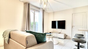 A modern living room with a beige sofa, a green throw pillow, a round coffee table, a black TV, and a bar stool. - Charming T2 with terrace and private parking (Champagne-au-Mont-d'Or)