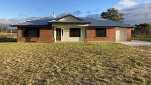 A modern two-story house with a brick exterior and a metal roof, surrounded by a grassy yard. - The Farm. Entire house country stay (Applethorpe)