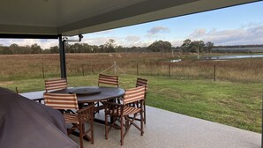 An outdoor patio with a round wooden table and striped chairs, overlooking a grassy field and a body of water. - The Farm. Entire house country stay (Applethorpe)