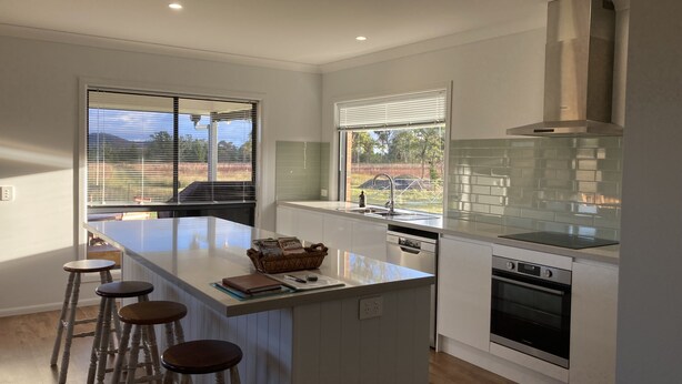 A modern kitchen with a central island, bar stools, a built-in oven, and a view of the outdoors. - The Farm. Entire house country stay (Applethorpe)