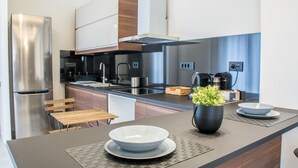 Een moderne keuken met roestvrijstalen apparatuur, een houten eettafel en een centraal keukenblok met een wasbak en een potplant.