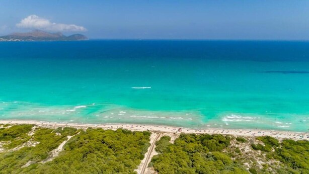 An aerial view of a coastal area with a beach, clear turquoise waters, and a small boat in the distance.