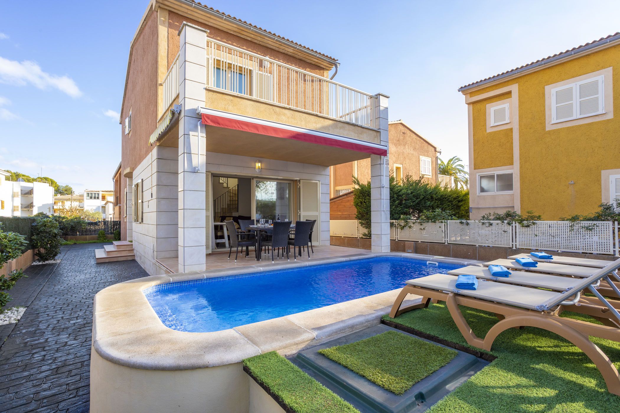 Una casa de dos pisos con piscina, mobiliario exterior y un patio.
