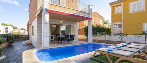 Una casa de dos pisos con piscina, mobiliario exterior y un patio.