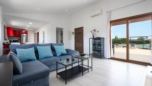 Una sala moderna con un sofá gris, una mesa de centro de vidrio y una zona de cocina con armarios rojos.