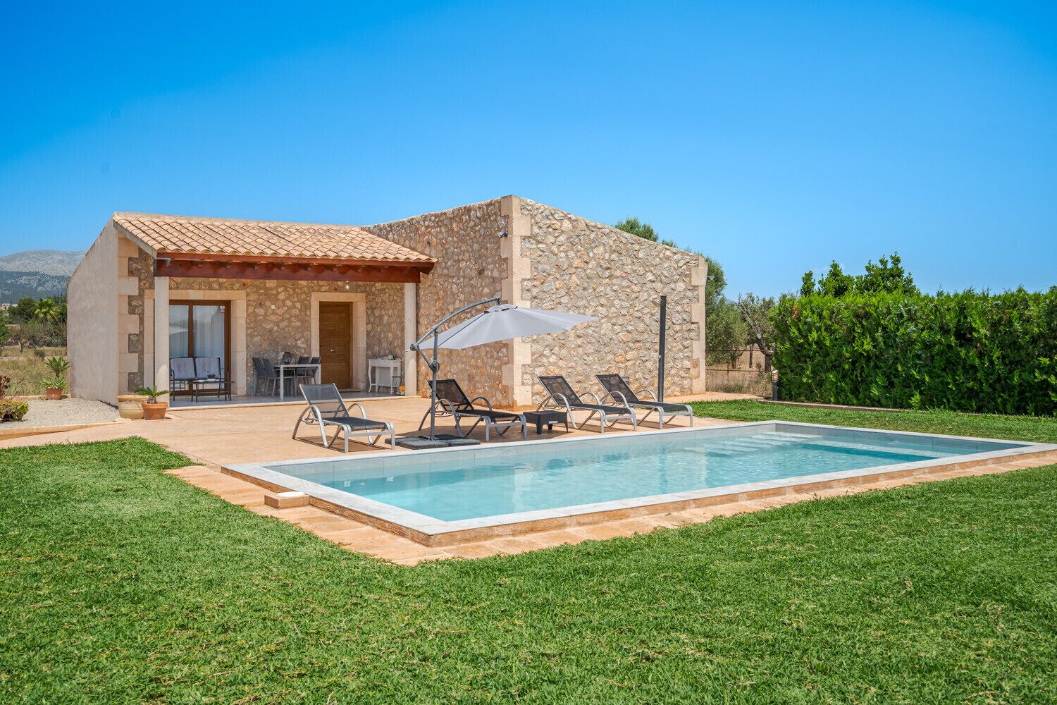 A stone house with a swimming pool, outdoor seating, and a clear view of the mountains.