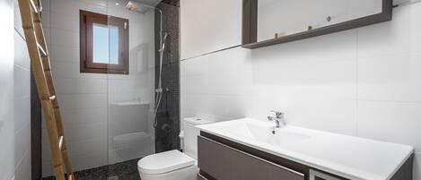 Uma casa de banho moderna com chuveiro, sanita e lavatório.