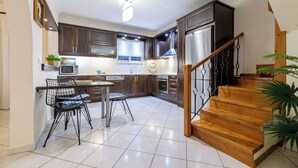 A modern kitchen with dark wooden cabinets, stainless steel appliances, and a wooden staircase. - Diogenis House (Zakynthos)