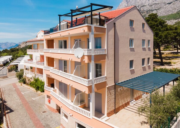 A multi-story building with balconies, a flat roof, and a view of mountains.