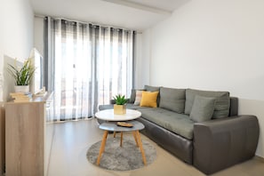 A modern living room with a grey sofa, a round coffee table, a small wooden side table, and a potted plant.