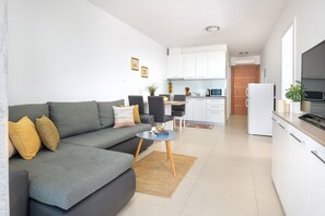 A modern living room with a grey sofa, a small round coffee table, and a kitchen area with white cabinets and a microwave.