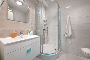 A modern bathroom with a glass-enclosed shower, a white sink with a wooden soap holder, and a white toilet.