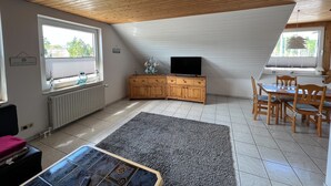 Une pièce chaleureuse avec un plafond en pente, des meubles en bois, une télévision et une table à manger avec des chaises.