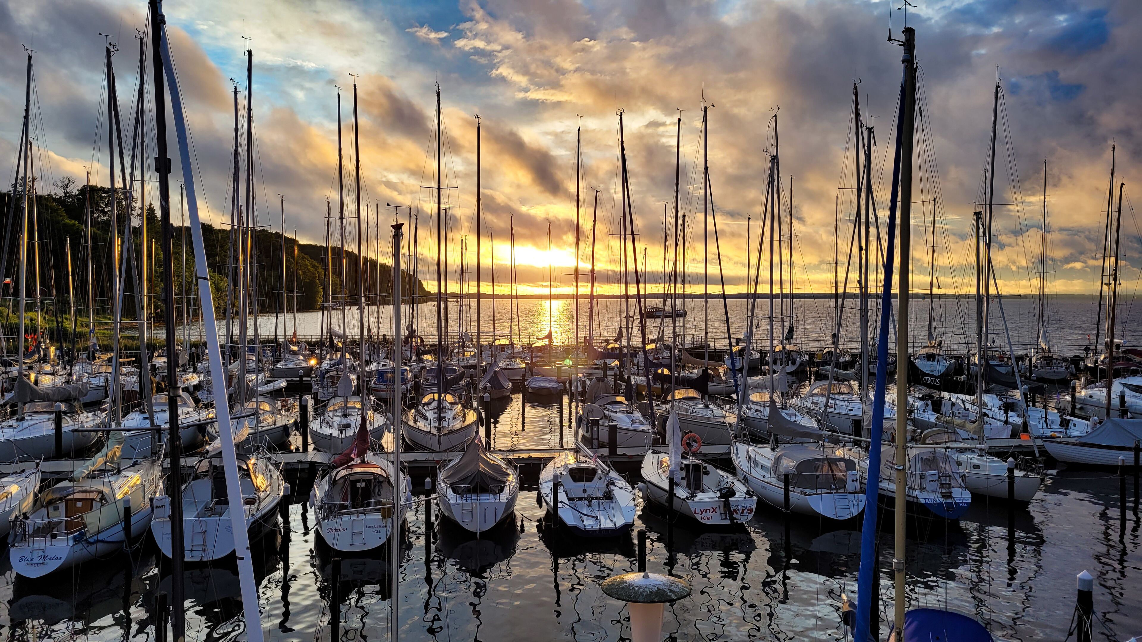 Een jachthaven met verschillende boten afgemeerd, omringd door water en een heuvelachtig landschap.